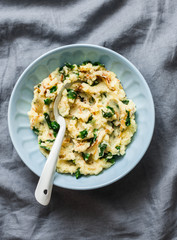 Mashed potatoes with spinach and crispy fried onions on a grey background, top view. Delicious side dish or vegetarian meal