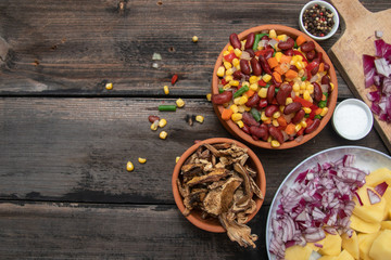 Mixture of vegetables, dried boletus mushrooms, sliced potato, red onion sliced and whole on a cutting board and spices, on old rustic wooden table. With copy space.