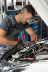 View from side of serious mechanic in uniform and protective gloves fixing motor of car in auto service. Professional worker repairing broken vehicle with wrench. Concept of maintenance.