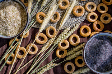 Flat lay with a lot of bagels, wheat spikelets, sesame seeds and poppy seeds on the table. Close up, flat lay