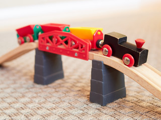 Wooden toy train running on miniature railroad bridge. The black engine pulling colorful cars on the floor. Educational toys for children in preschool and kindergarten.