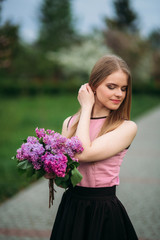Blond hair girl hold a bouquet of lilac in hands. Outside