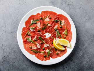 Beef Carpaccio cold appetizer with parmesan, capers and arugula on white plate