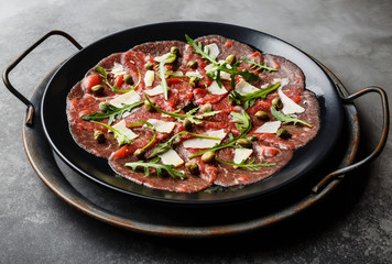 Beef Carpaccio cold appetizer with parmesan, capers and arugula on black plate