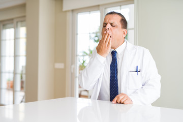 Fototapeta premium Middle age doctor man wearing medical coat at the clinic bored yawning tired covering mouth with hand. Restless and sleepiness.