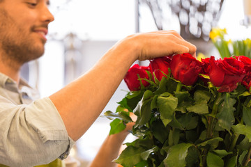 small business, sale and floristry concept - close up of florist or seller setting red roses at flower shop