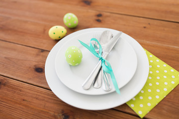 easter, holidays, tradition and object concept - green colored egg in cup holder, plates and cutlery on table at home