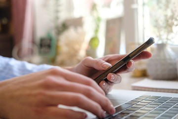 Woman using smart phone and laptop, female hands using smart phone in interior at home, woman at workplace using technology. Female hands on the keyboard. Close up