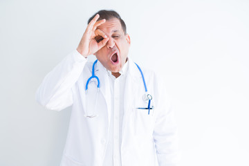 Middle age doctor man wearing stethoscope and medical coat over white background doing ok gesture shocked with surprised face, eye looking through fingers. Unbelieving expression.