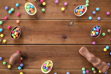 easter, sweets and confectionery concept - chocolate eggs, bunny and candy drops on wooden background