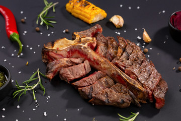 Medium rare grilled Steak Ribeye Black Angus with corn and rosemary on serving on black background