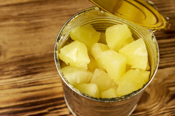 Opened tin can of pineapple pieces on wooden table