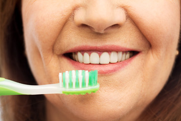 dental care and hygiene people concept - close up of smiling senior woman with toothbrush brushing her teeth over white background