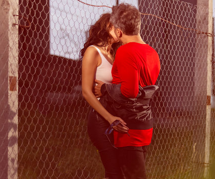 the guy hugs the girl kissing her standing by the iron fence