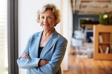 Portrait Of Smiling Senior Businesswoman In Modern Office Standing By Window