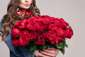 Close up of huge and elegant bouquet of red roses. Brunette woman with full lips and long hair holding flowers. Stylish lady in big gold and red earrings getting presents on her birthday.