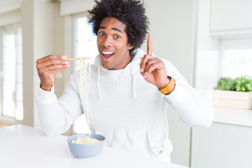 African American man eating asian noodles using chopsticks at home surprised with an idea or question pointing finger with happy face, number one