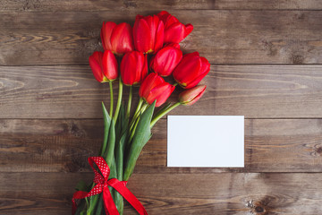 Spring flowers. Bouquet of Red tulips with card for text on brown wooden background. Mother's Day and Valentines Day concept. Flat lay