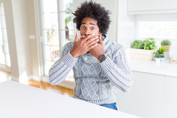 African American man wearing winter sweater shocked covering mouth with hands for mistake. Secret concept.