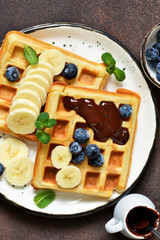 Breakfast time. Homemade waffles with banana, blueberry and chocolate spread on a kitchen table.