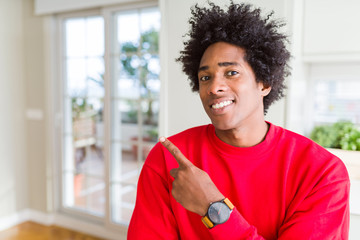 African American man wearing casual red sweatshirt cheerful with a smile of face pointing with hand and finger up to the side with happy and natural expression on face