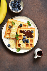 Fototapeta na wymiar Breakfast time. Homemade waffles with banana, blueberry and chocolate spread on a kitchen table.