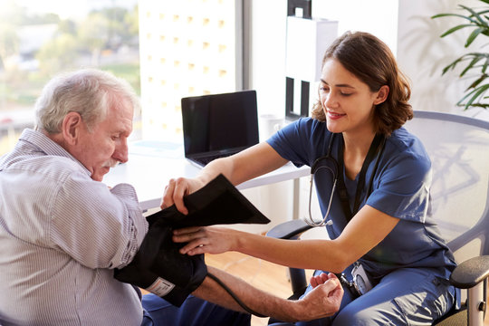 Nurse Wearing Scrubs In Office Checking Senior Male Patients Blood Pressure