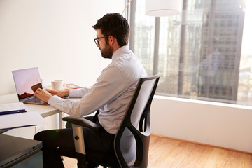 Businessman Sitting At Desk Working On Laptop In Modern Office