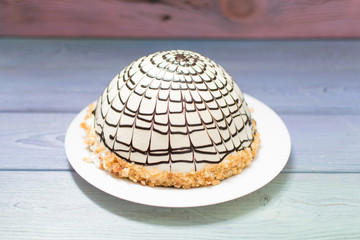 Cream cake sprinkled with spherical chocolate on a wooden background.