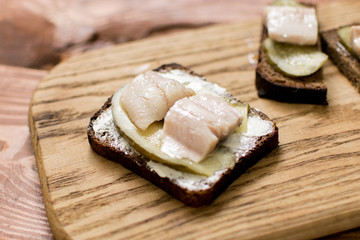 Sandwich from black bread with butter and herring on a wooden background.