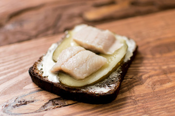 Sandwich from black bread with butter and herring on a wooden background.