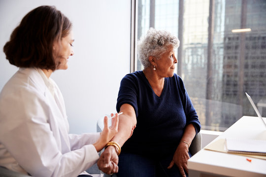 Senior Woman Being Vaccinated With Flu Jab By Female Doctor In Hospital Office