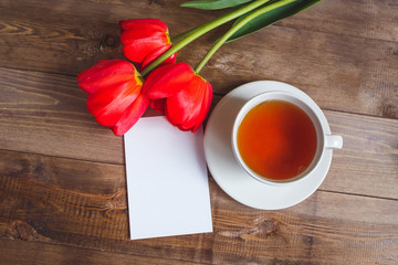 Spring flowers. Bouquet of Red tulips with tea cup and present card on brown wooden background. Mother's Day and Valentines Day concept. Top view