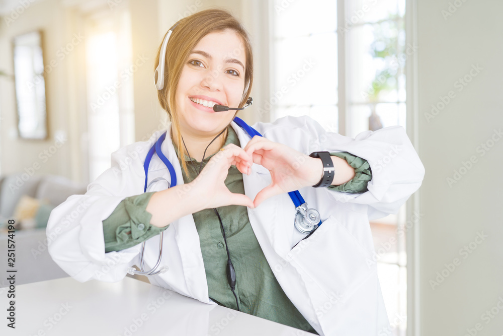 Sticker Beautiful young doctor woman wearing headset smiling in love showing heart symbol and shape with hands. Romantic concept.