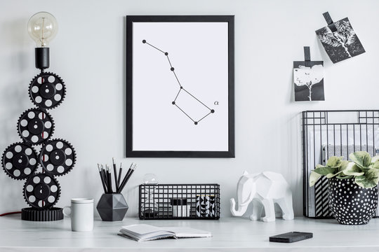 Stylish black and white home decor mock up. Creative desk with blank picture frame or poster, desk objects, office supplies, elephant figure and plants in design pots on a white background.