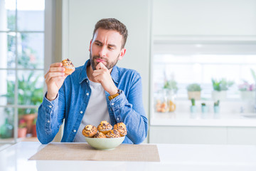 Handsome man eating chocolate chips muffin serious face thinking about question, very confused idea