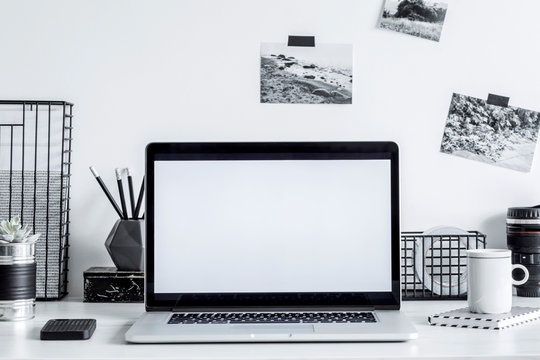 Stylish black and white home decor with mock up laptop screen. Creative desk with photos, desk objects, office supplies, cup of coffee on a white background. Open workspace for freelancer. 