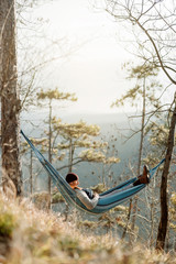Young happy man relaxing lying in hammock on top of mountain.