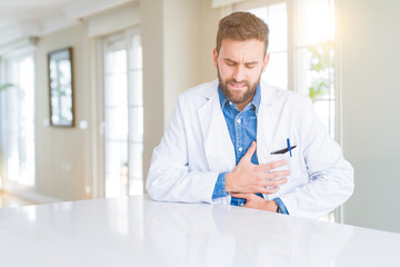 Handsome doctor man wearing medical coat at the clinic with hand on stomach because nausea, painful disease feeling unwell. Ache concept.