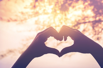Female hands heart shape on nature bokeh sun light flare and blur leaf abstract background.