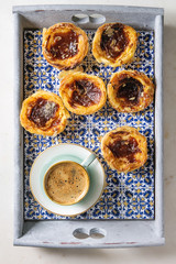 Traditional Portuguese egg tart dessert Pasteis Pastel de nata in classic tile tray with cup of black coffee. Flat lay, space