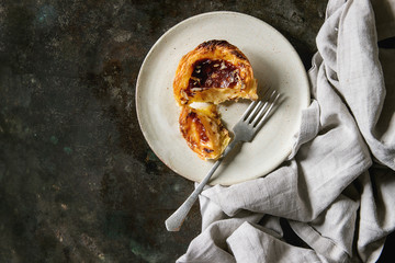 Traditional Portuguese egg tart dessert Pasteis Pastel de nata on ceramic plate with fork and cloth over dark metal background. Flat lay, space