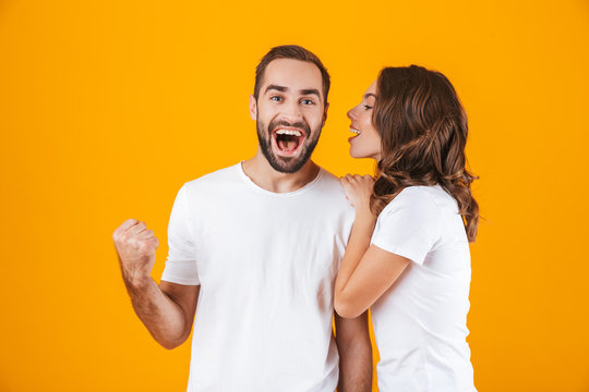 Image of brunette woman whispering secret or interesting gossip to man in his ear, isolated over yellow background