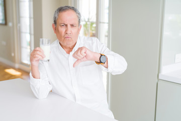 Handsome senior man drinking a glass of fresh milk at breakfast with angry face, negative sign showing dislike with thumbs down, rejection concept