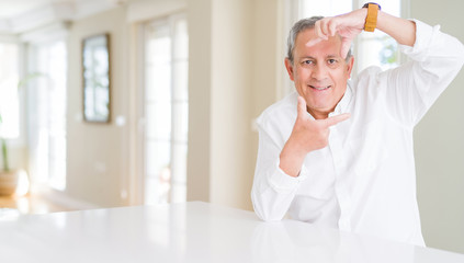 Handsome senior man at home smiling making frame with hands and fingers with happy face. Creativity and photography concept.