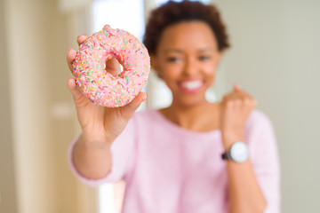 Young african american woman eating pink sugar donut screaming proud and celebrating victory and success very excited, cheering emotion