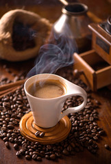 cup of coffee and coffee beans in a sack on dark background, top view