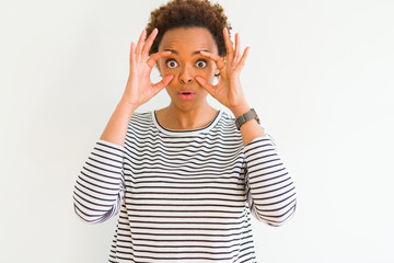 Young beautiful african american woman wearing stripes sweater over white background Trying to open eyes with fingers, sleepy and tired for morning fatigue