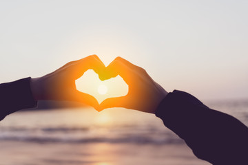 Female hands heart shape on nature bokeh sun light flare wave and blur tropical beach abstract...