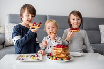 Sweet toddler birthday boy and his brothers, eating belgian waffle with raspberries, blueberries,...